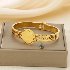 Detail of gold coin bracelet with blue evil eye charm and Greek key pattern on jewelry box
