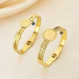 Detailed shot of golden coin relief bangles with Greek key patterns and evil eye charms