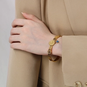 Macro shot of gold coin bracelet with evil eye charm worn over a beige suit sleeve