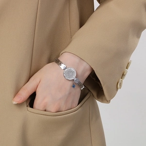 Detailed view of silver titanium steel bracelet with evil eye and coin pendant on wrist