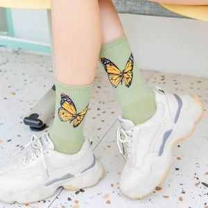 Detail of green mid-calf cotton socks with butterfly pattern worn with white sneakers