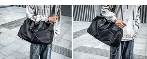 Street style view of a black nylon travel bag with handles and a detachable shoulder strap