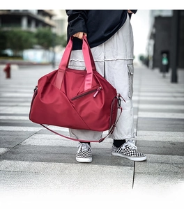Close-up of burgundy nylon travel bag with handles and detachable shoulder strap on street