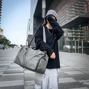 Modern grey-green duffel bag with black straps used in an urban outdoor lifestyle setting