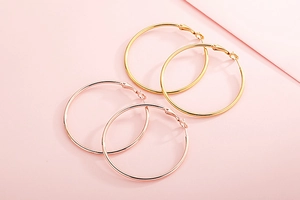 Détail de créoles dorées et or rose avec finition polie sur un fond rose doux