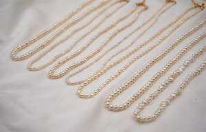 Macro view of assorted freshwater pearl necklaces with golden lobster clasps on white fabric
