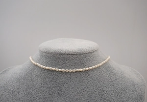Detailed close-up of a white mini freshwater pearl necklace on a velvet display stand