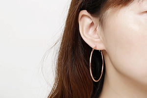 Gros plan de grandes boucles d'oreilles créoles minimalistes en or rose poli portées