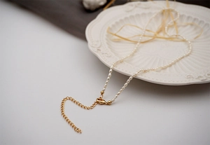 Detailed macro shot of white rice pearls featuring a gold alloy lobster clasp and chain