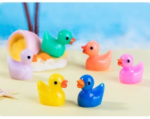 Group of six colorful miniature resin duck figurines on a sandy beach background