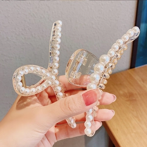 Close-up of a clear acrylic hair claw clip decorated with white pearls being held