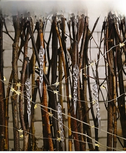 Close-up of clear acrylic icicle ornaments hanging with warm star lights on a branch