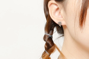 Close-up of polished silver dolphin stud earrings worn by model with braided hair