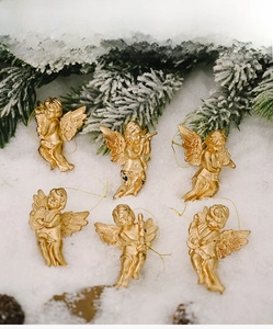 Set of six golden musical angel ornaments displayed on snow with pine branch background