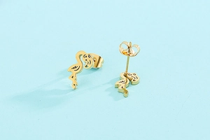 Detail view of golden flamingo stud earrings set on a clean blue surface backdrop