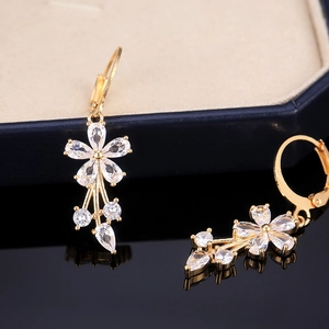 Macro detail of gold flower drop earrings with sparkling cubic zirconia on a black mirror