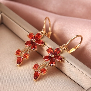 Elegant gold flower earrings with red pear-cut zircons and champagne silk backdrop