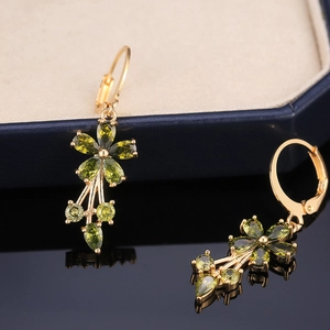 Macro shot of gold floral earrings with olive green zirconia and cascading tassels