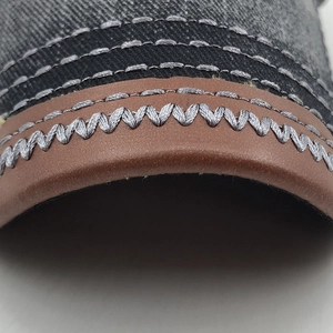 Vue macro d'une casquette en denim avec coutures de précision en Z sur bordure en cuir
