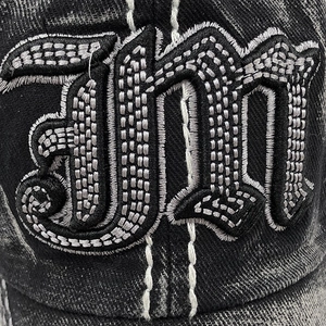 Détail macro de broderie gothique 3D sur casquette de baseball en jean noir délavé