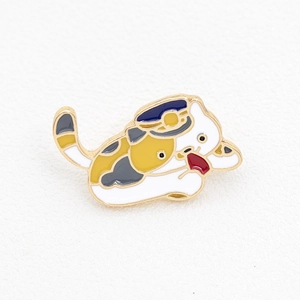 Detail of cute cat enamel pin with blue hat and golden metal edges on white background