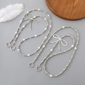 Detail of silver pearl phone strap featuring elegant beaded bows and metal clasps