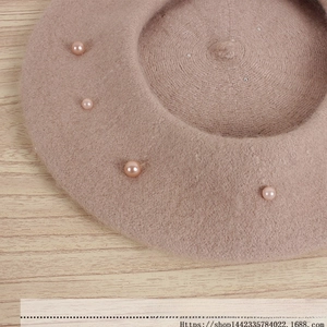 Detail of tan woolen beret featuring decorative pink pearls on textured fabric