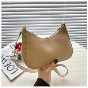 Detail of a beige leather hobo bag with gold hardware and wide strap in a modern setting