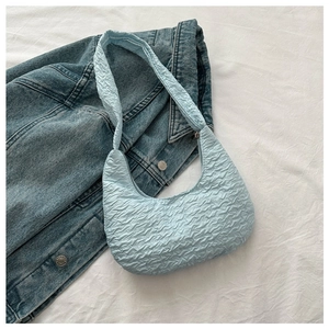 Close-up of light blue pleated dumpling bag on denim jacket backdrop for a casual look