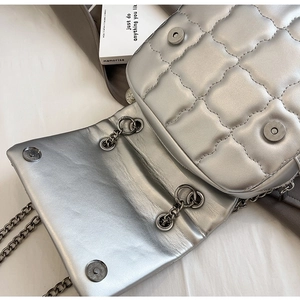 Detailed close-up of quilted silver leather bag with metallic chain and magnetic buckle