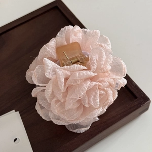 Macro view of a light pink tulle rose flower hair claw clip on a dark wooden tray