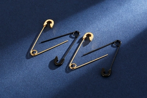 Macro detail of gold and black safety pin earrings on a textured blue surface