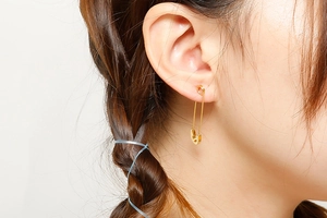 Close-up of a gold safety pin earring worn by a model showcasing sleek metallic texture