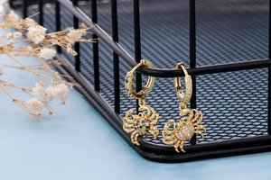Close-up of golden crab earrings with colorful zircon stones on a black grid