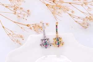 Detail of frog-shaped earrings with colorful zircon stones on a white wavy plate