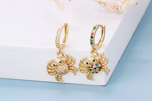 Detail of gold crab earrings with colorful cubic zirconia on a white display block