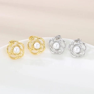Macro detail of camellia pearl earrings in gold and silver finish on white porcelain plate