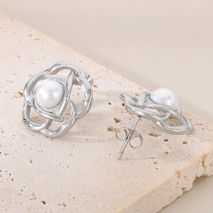 Macro view of silver camellia earrings with white pearl detail on textured stone