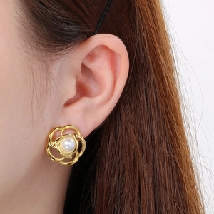Elegant gold openwork camellia earrings with pearl center shown on a model's ear