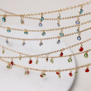 Layered gold chain jewelry featuring vibrant red blue and green gemstone pendants