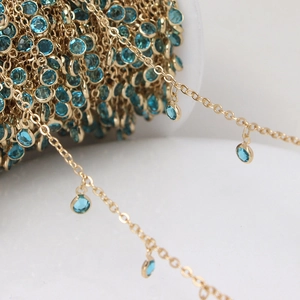 Macro detail of gold plated jewelry chain with round sky blue gemstone charms