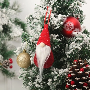 Detail of a Christmas gnome hanging on a snowy tree with a red knitted hat and white beard