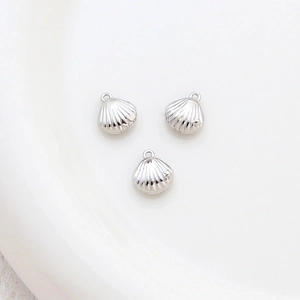 Detailed view of three silver shell-shaped pendants with small loops on white ceramic