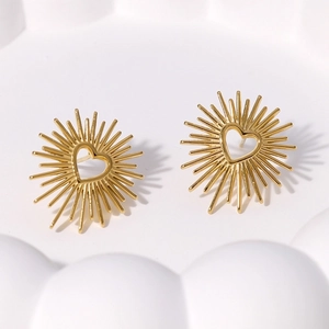 Pair of gold heart-shaped stud earrings with sunburst design on a white ceramic tray