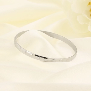 Detailed view of silver titanium steel bangle with heart indentations on soft fabric
