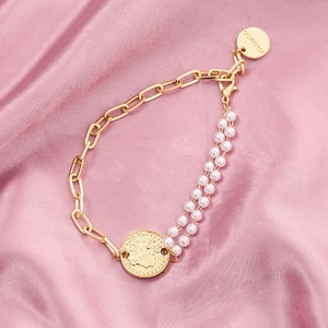 Detail of pearl bracelet with gold chain and vintage coin pendant on pink silk