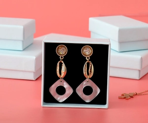 Detail of pink and gold seashell drop earrings inside a minimalist white jewelry box