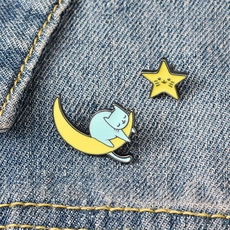 Dettaglio delle spille smaltate gatto-luna e stella su tessuto denim blu scuro