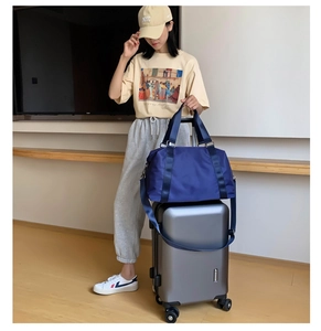 Waterproof navy nylon gym bag with detachable strap placed on silver luggage