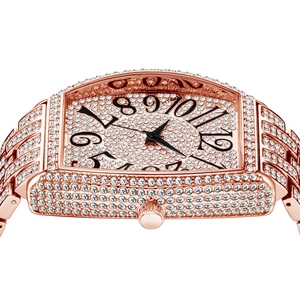 Detail of rose gold tonneau watch with iced out crystals and black numerals on white backdrop